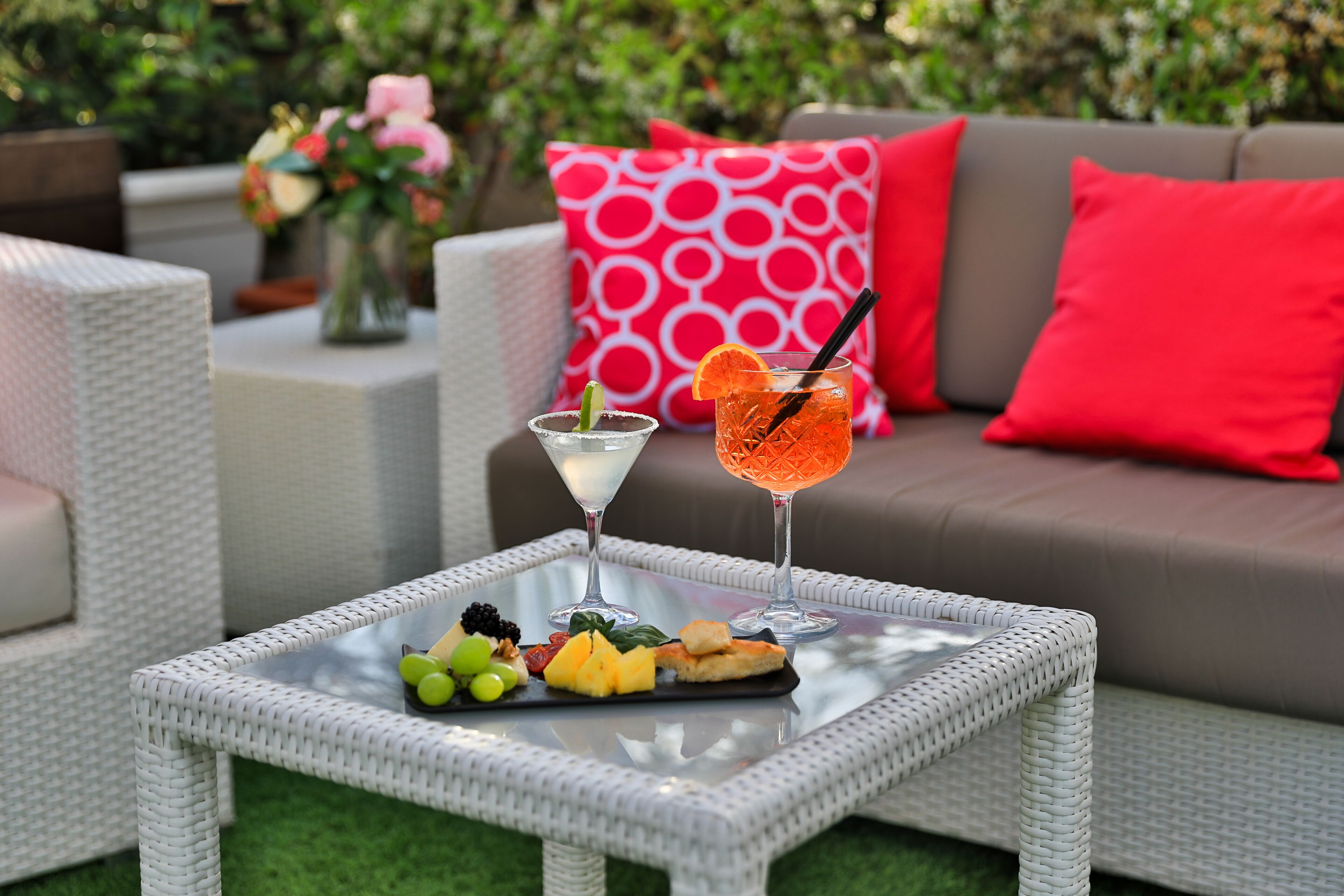 Une table en osier avec un plateau en verre, une assiette de fruits et deux boissons.