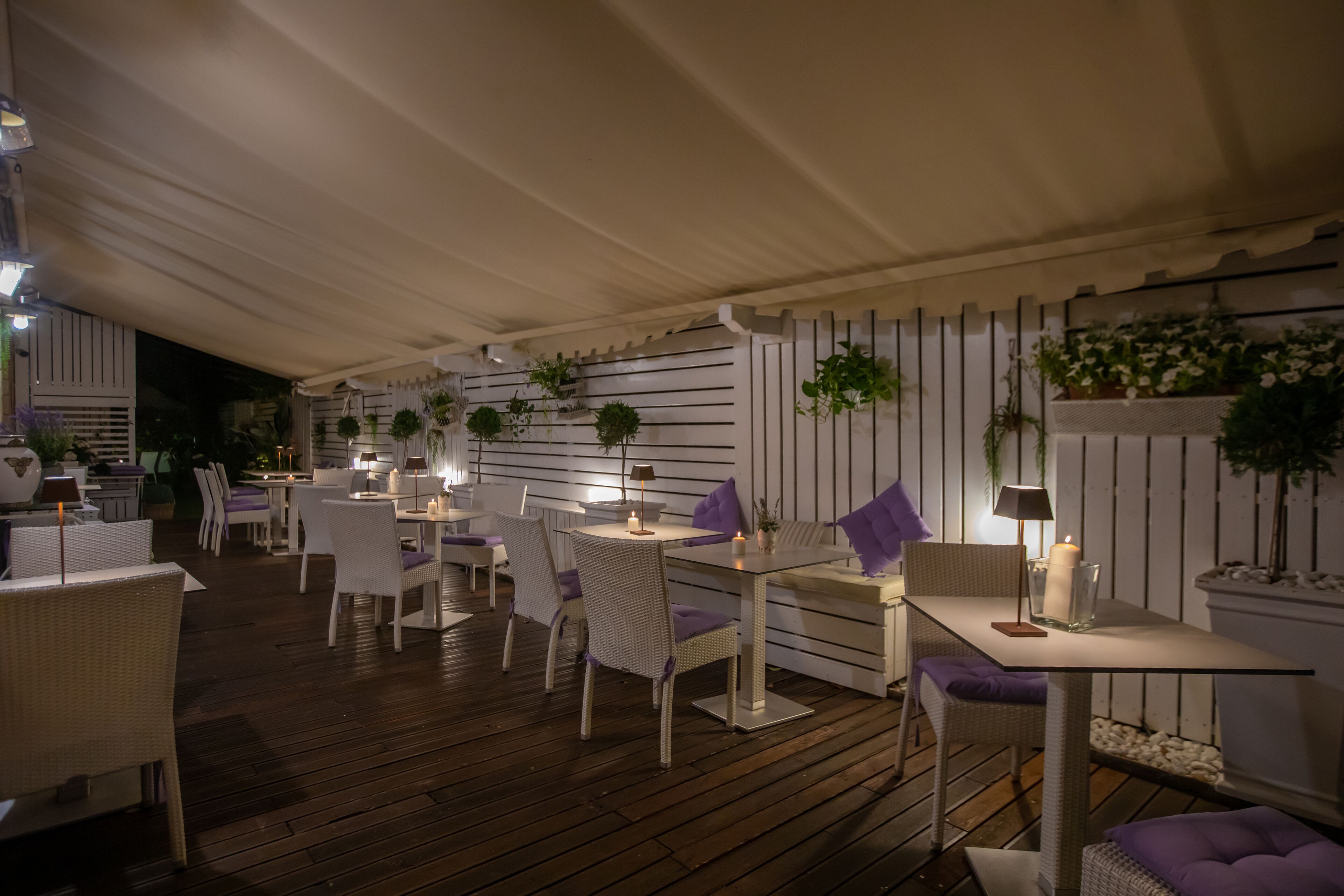 An outdoor dining area with white wicker furniture, tables, and chairs, under a white tent.