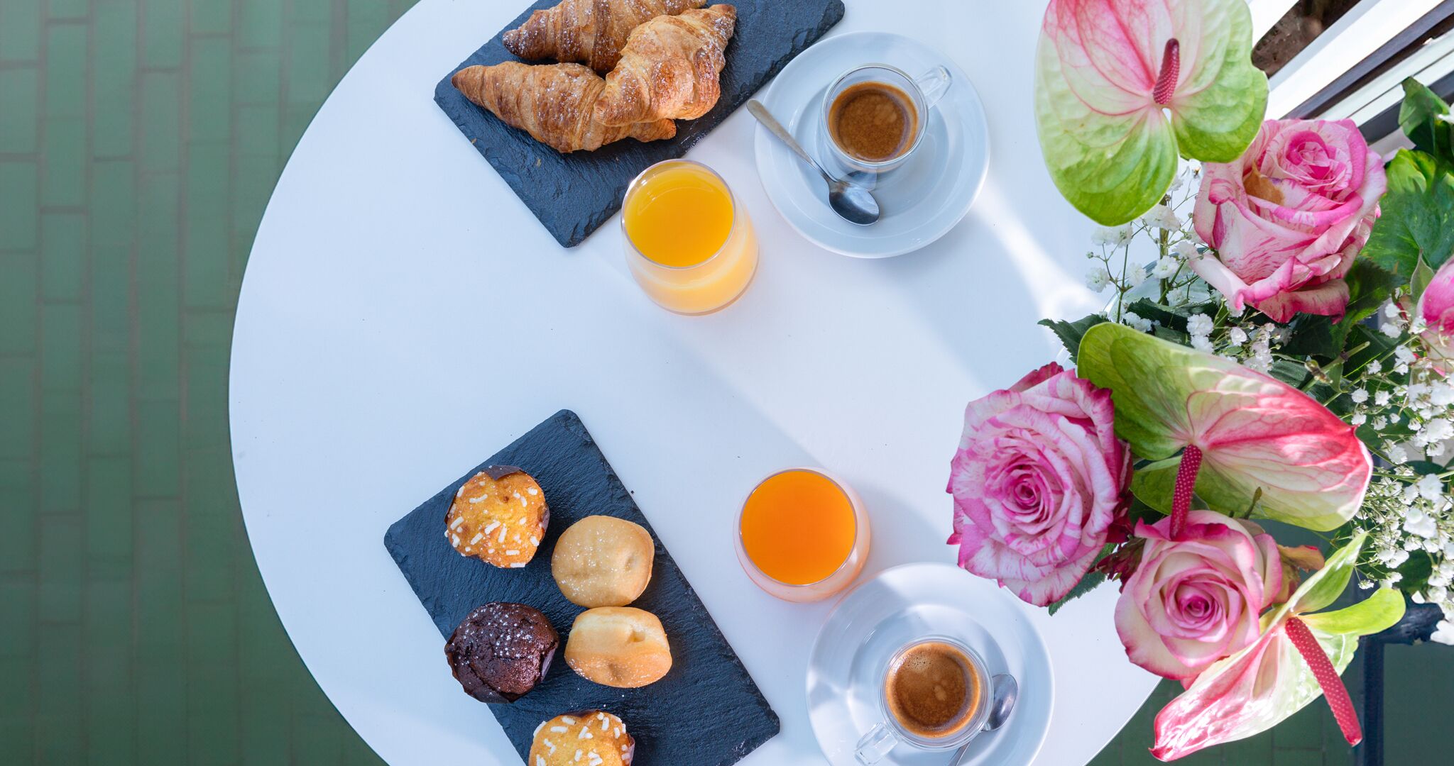 A round table with croissants, muffins, and coffee, accompanied by a flower arrangement.