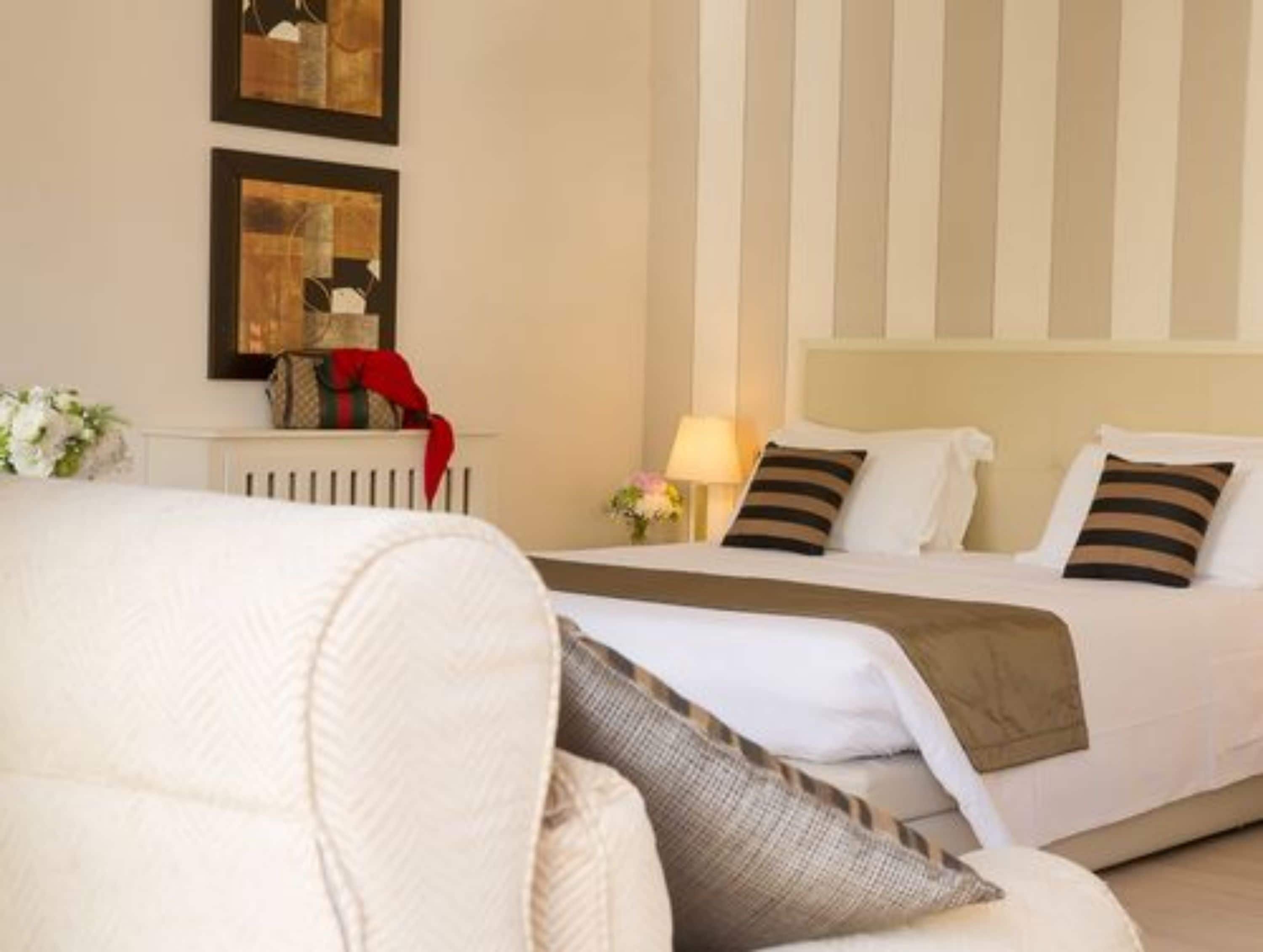 A hotel room with a bed, a chair, and two framed artworks on the wall.