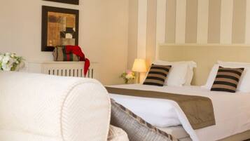 A hotel room with a bed, a chair, and two framed artworks on the wall.