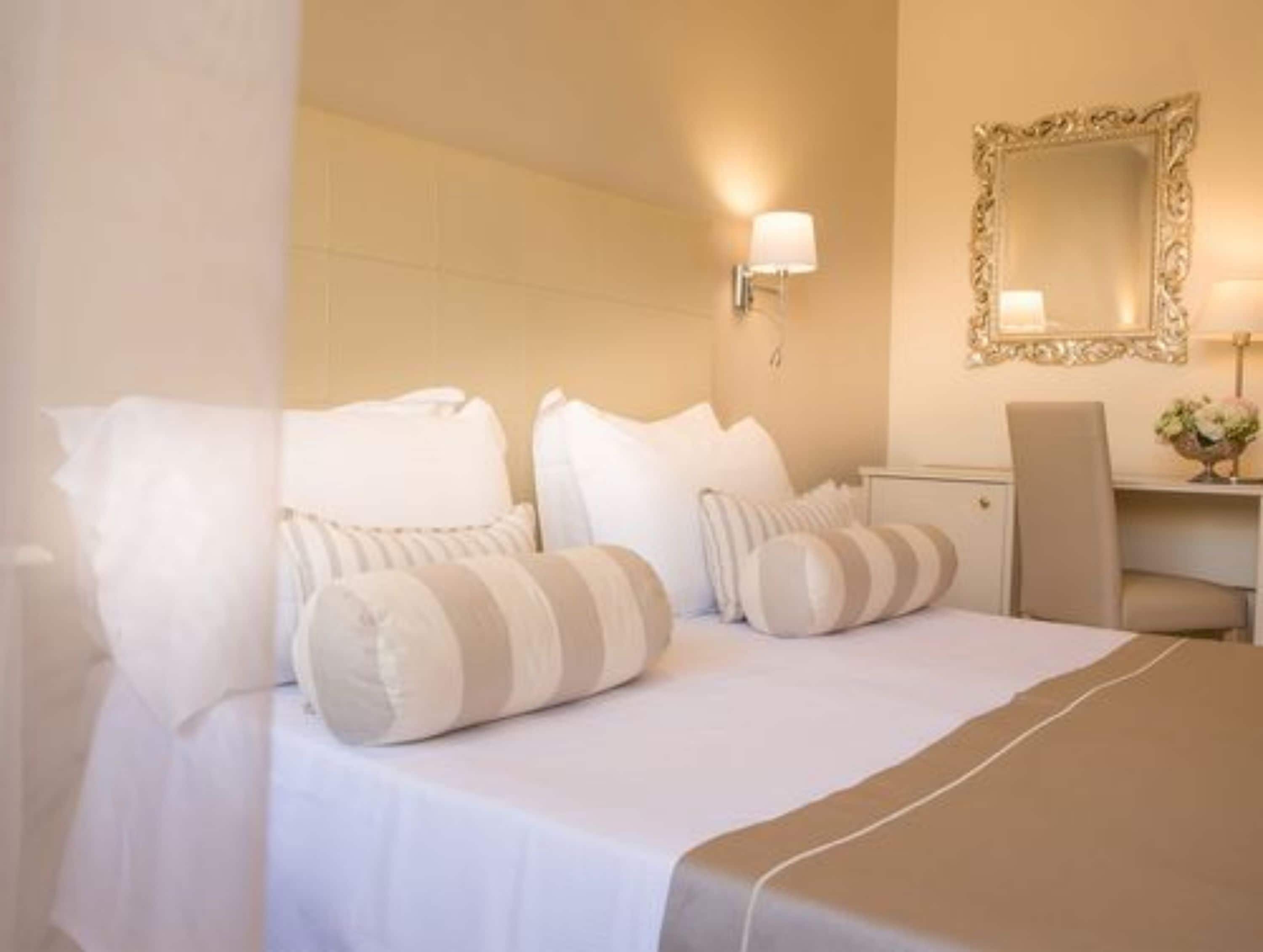 Une chambre d’hôtel avec un lit, des oreillers, une table de chevet, une lampe et un miroir.