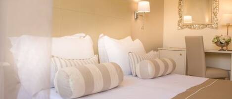 A hotel room with a bed, pillows, a nightstand, a lamp, and a mirror.