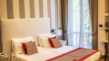 A hotel room with a large bed, a bedside table, a red chair, and a window with curtains.