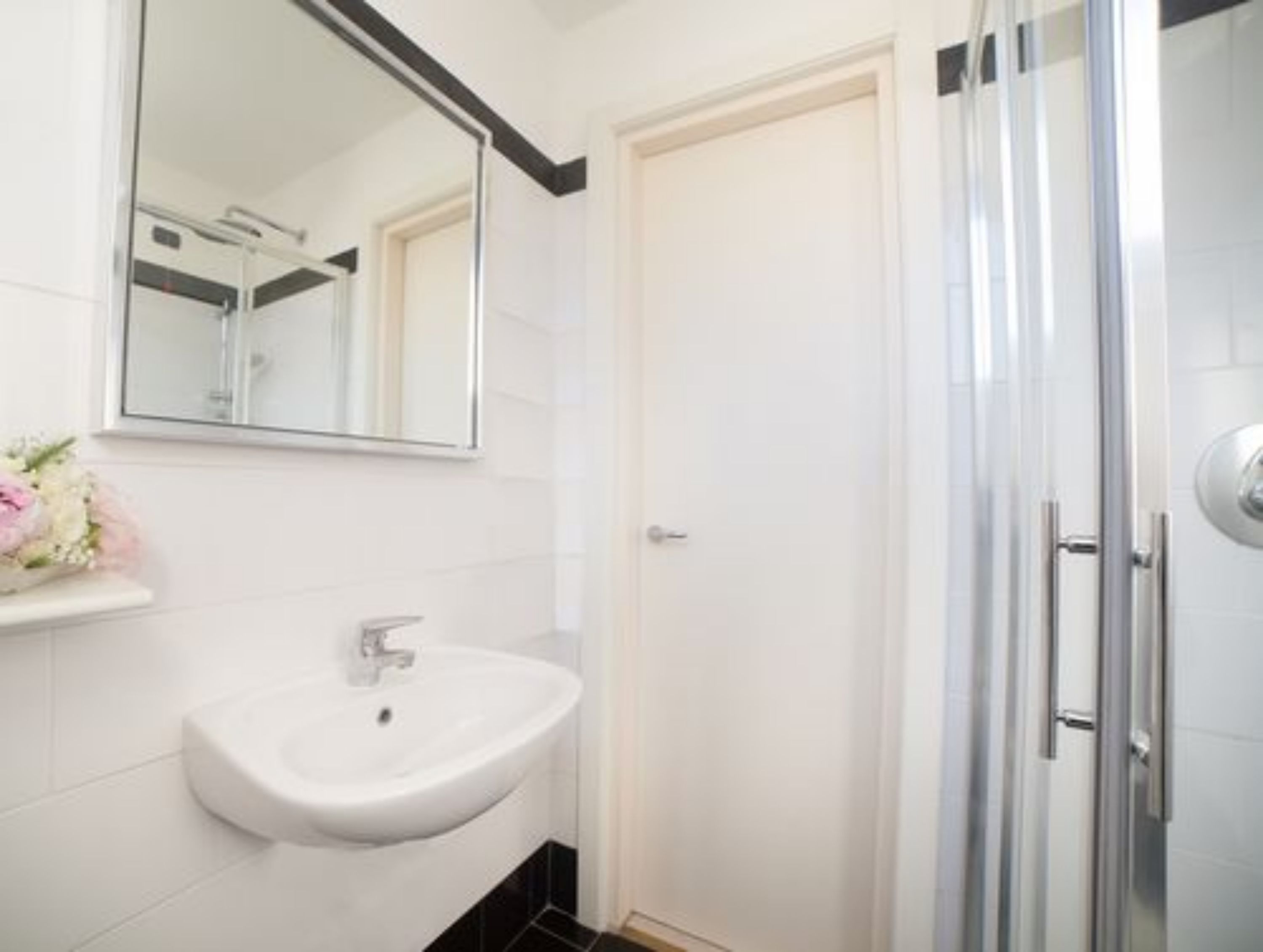Une salle de bain avec un lavabo blanc, un miroir et une douche.