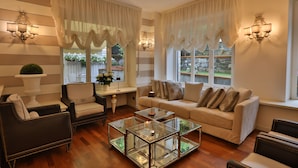 A living room with striped walls, a sofa, armchairs, a glass coffee table, and two windows with curtains. - Hotel Tigullio et de Milan (Santa Margherita Ligure)