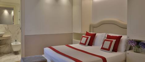 Un dormitorio moderno con una cama grande, mesitas de noche, un espejo y un baño con lavabo y bidé.