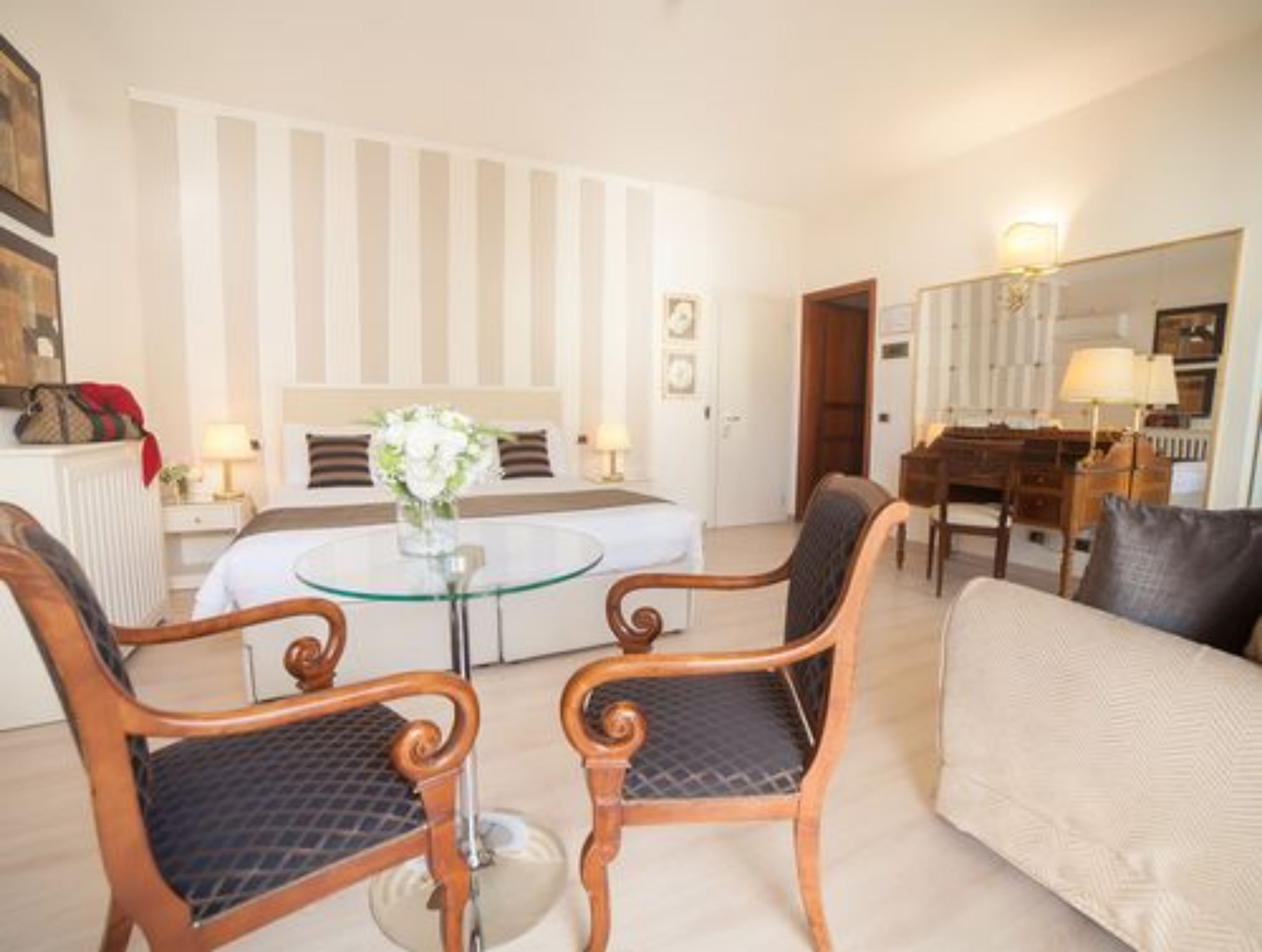 A hotel room with a bed, a round glass table, two upholstered chairs, a sofa, a dresser, and a mirror.
