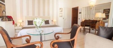 Habitación de hotel con cama, una mesa redonda de vidrio, dos sillones tapizados, un sofá, un aparador y un espejo.