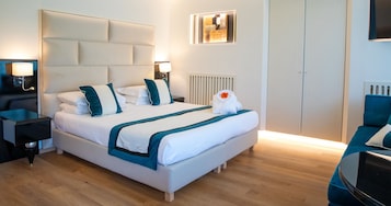 Una habitación de hotel moderna con una cama grande, mesitas de noche, un radiador y una zona de estar con una silla.
