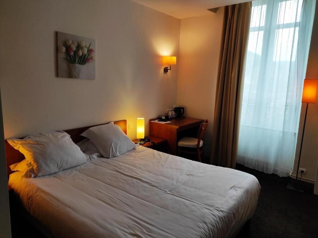 Ein Hotelzimmer mit Bett, Nachttischlampen, Schreibtisch mit Stuhl, einem Bild an der Wand und einem Fenster mit Vorhängen.