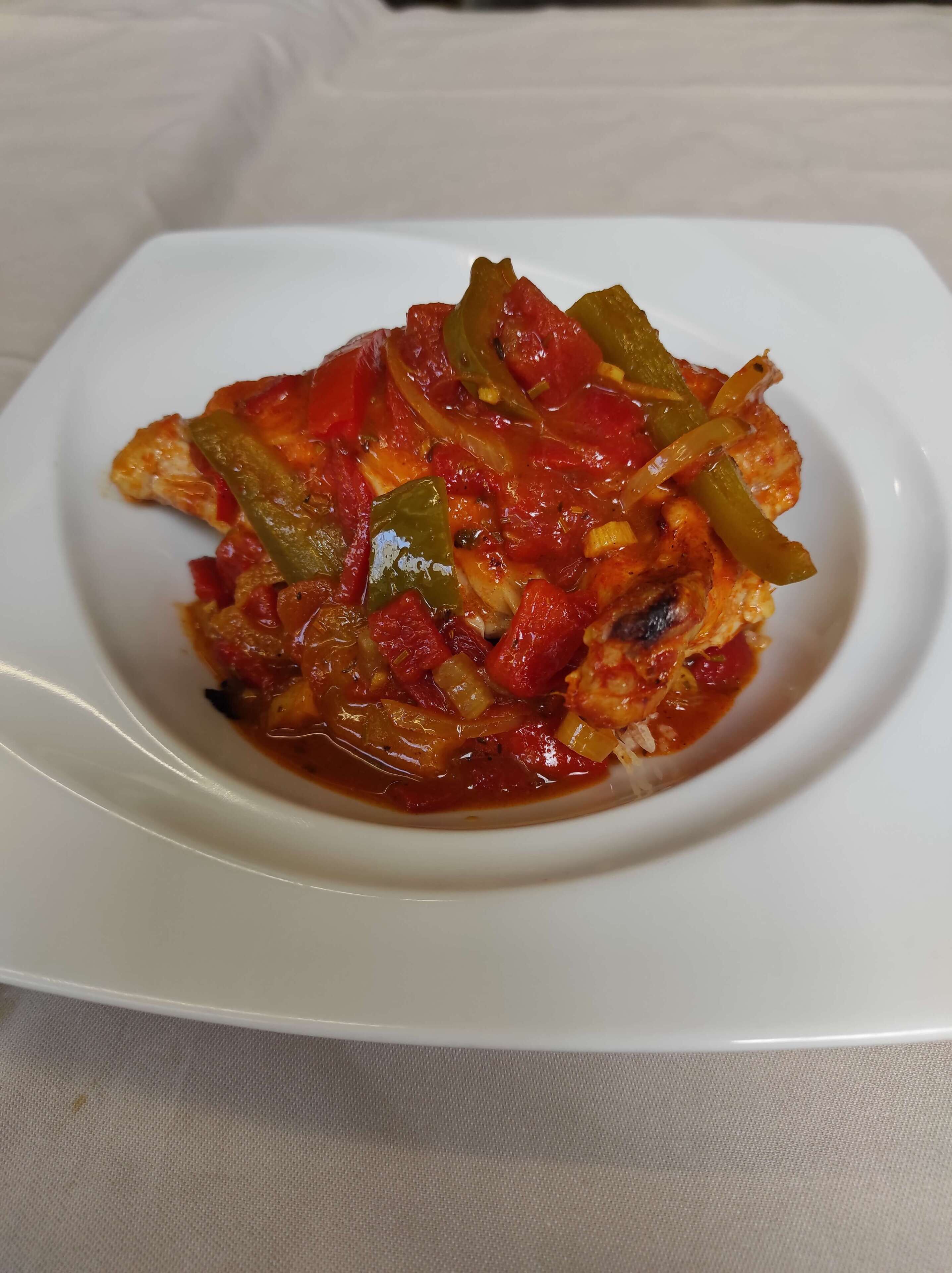 Ein weißer Teller mit einer Mahlzeit, möglicherweise Hähnchen, mit Gemüse und Soße.