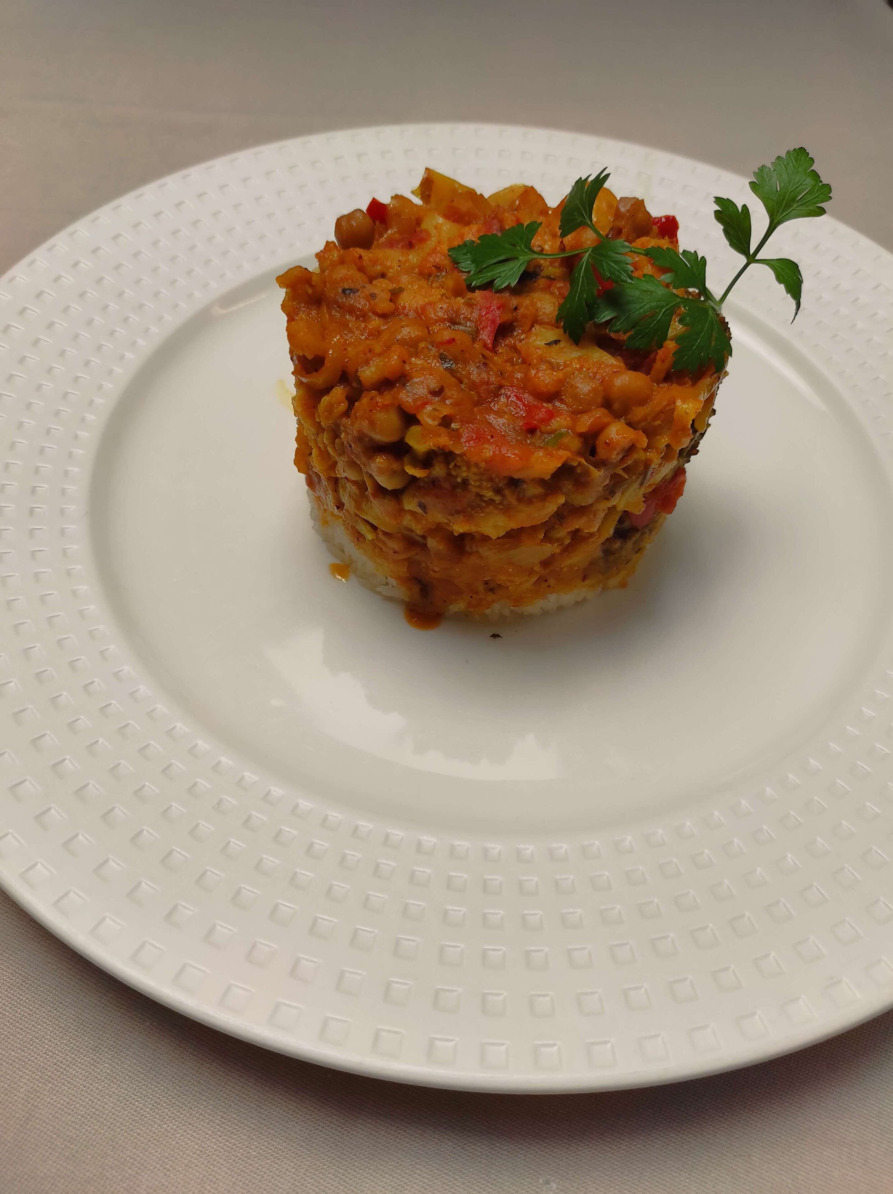 A white plate with a textured rim, holding a food item topped with parsley.