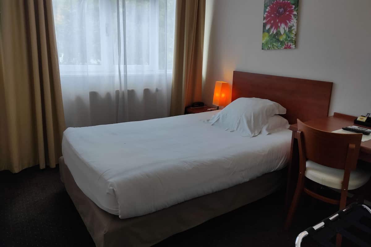 Una habitación de hotel con cama, escritorio, silla, lámpara y un cuadro en la pared.