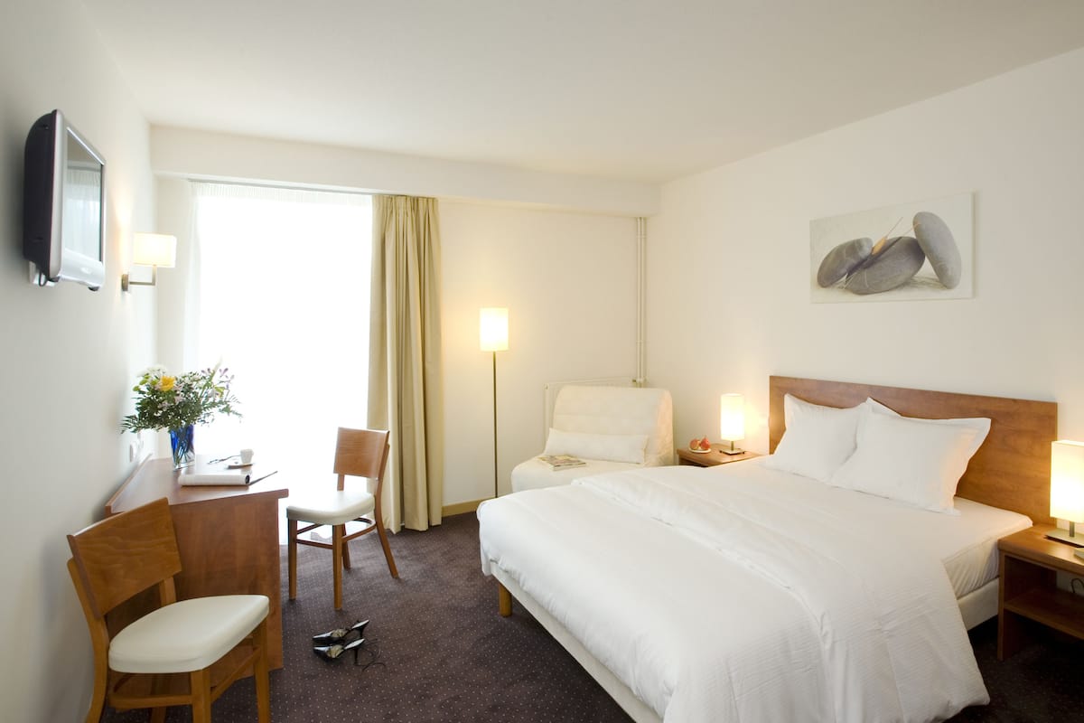 Habitación de hotel con cama, escritorio, silla, lámpara y un cuadro en la pared.