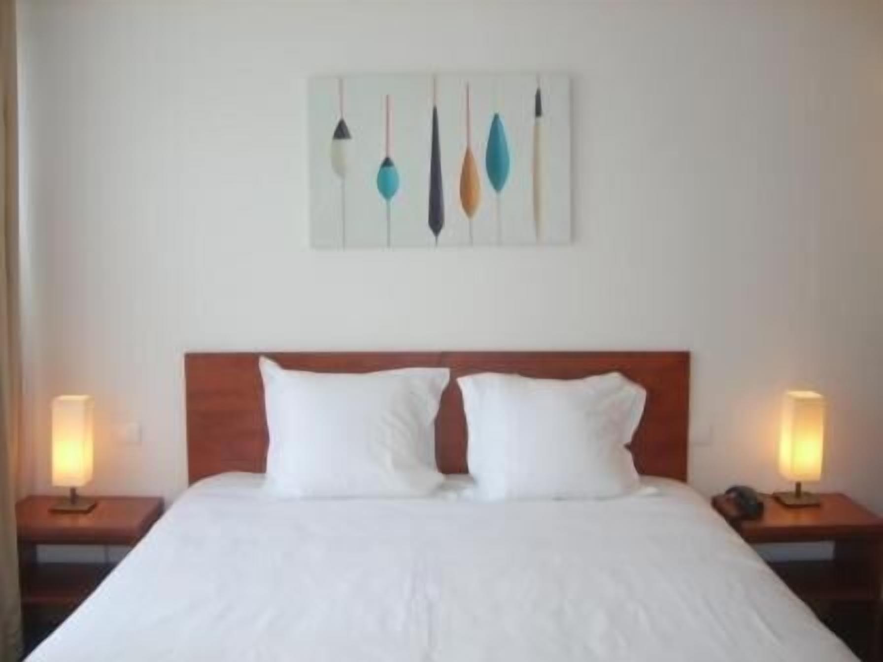 A hotel room with a large bed, two bedside tables, and a wall-mounted artwork.