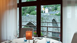 Ein Esstisch, gedeckt mit Tellern, Gläsern und Besteck, mit Blick auf eine malerische Landschaft aus Steinbrücke und üppigem Grün.