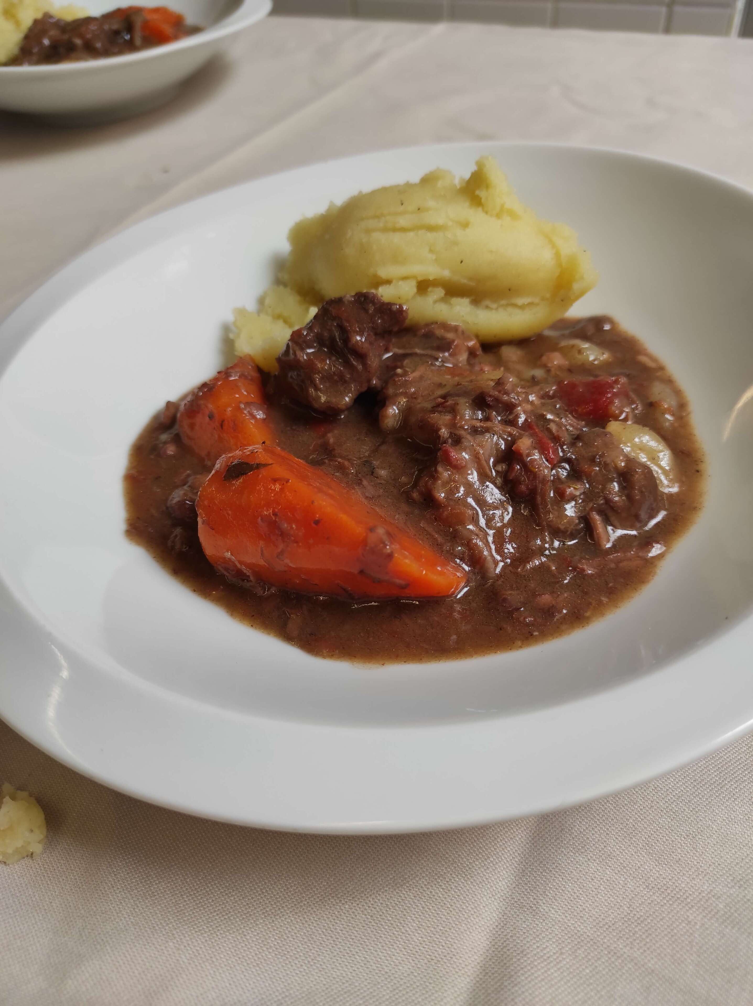 Ein Teller Rindfleischeintopf mit Karotten und Kartoffelpüree.