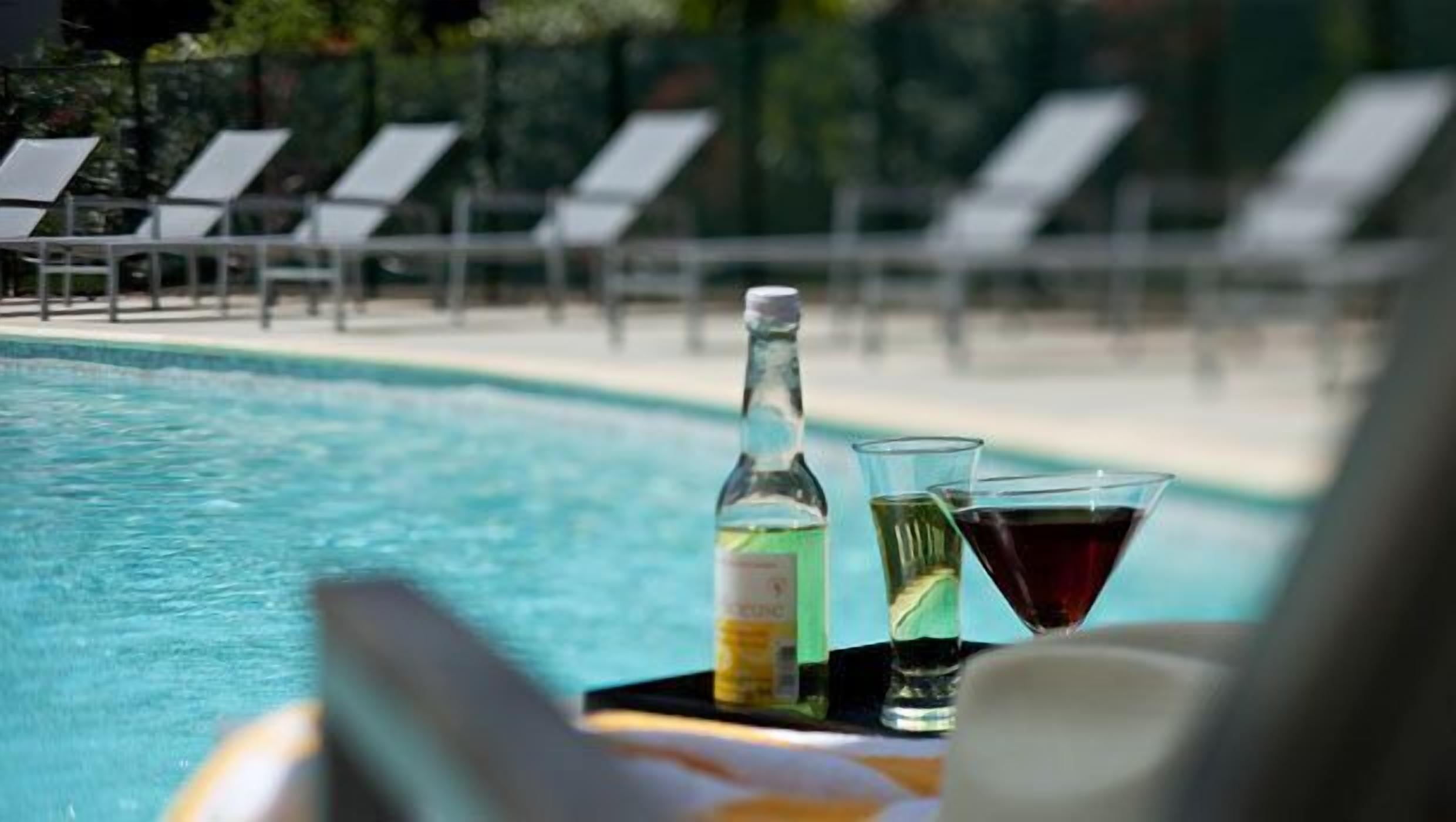 A poolside setting with lounge chairs and a table with a bottle and glasses.