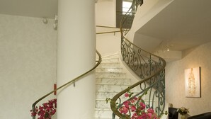 Eine мраморна́я лестница mit geschwungener Form, einer Handlauf und einem Blumentopf mit rosa Blüten.