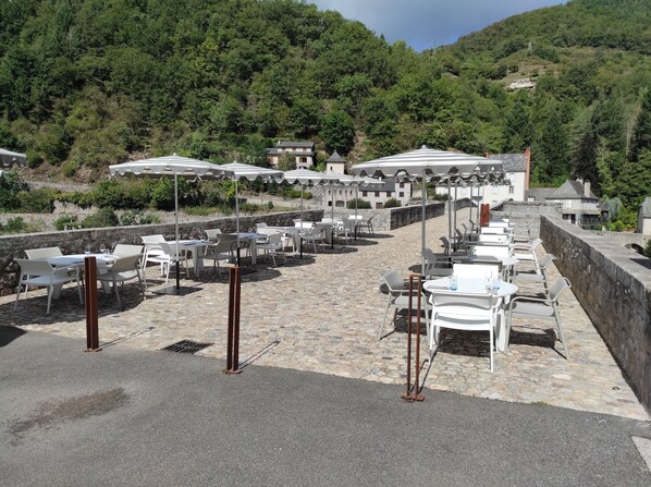 A terrace with outdoor seating, stone flooring, and a view of a hillside.