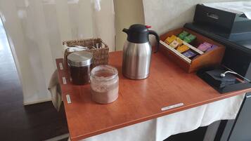 Ein Kaffee-Bereich mit einer Kaffeemaschine, einem Thermosbehälter und einem Kakao-Glas auf einem Holztisch.