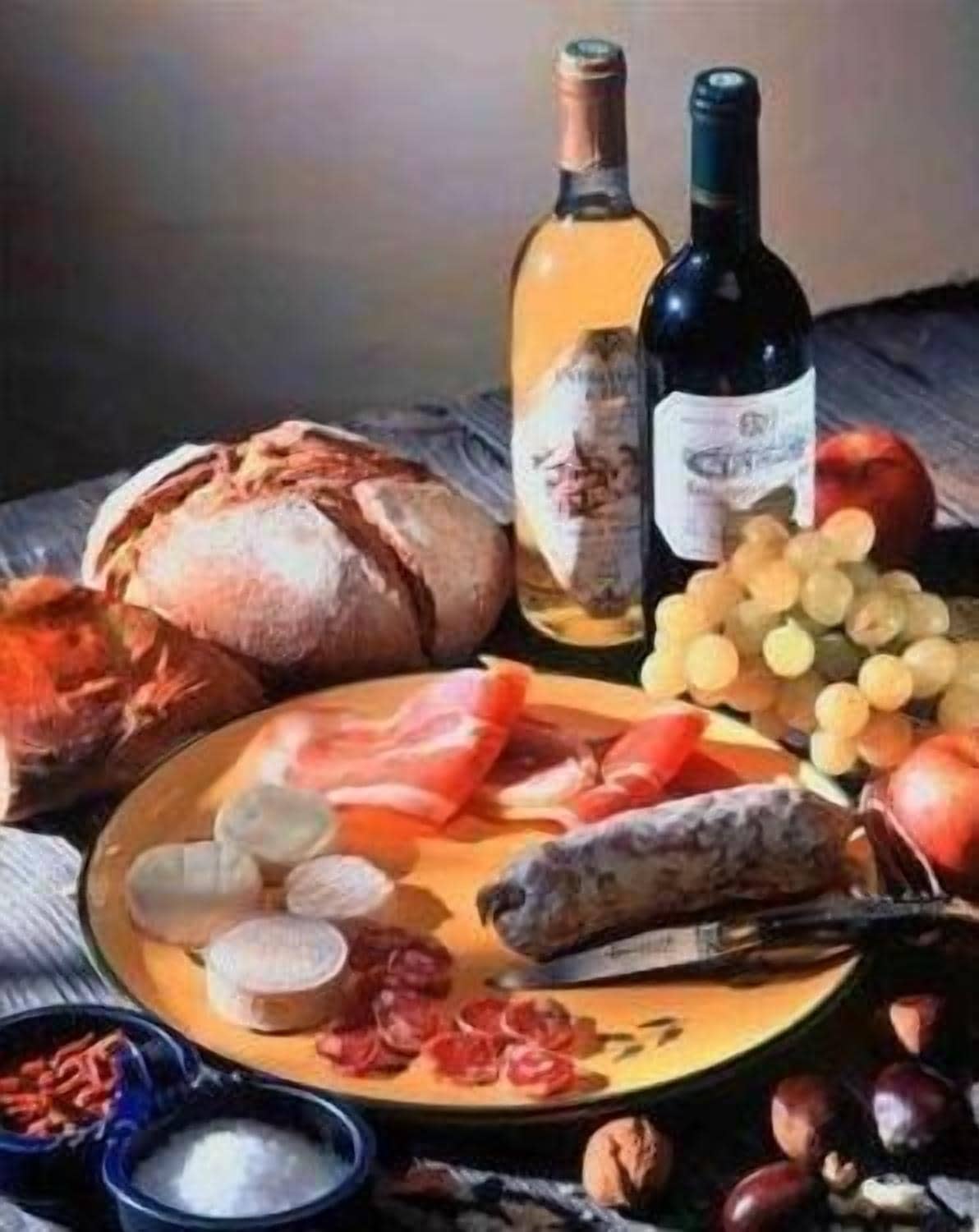 A table with various food items including bread, cheese, grapes, and a bottle of wine.