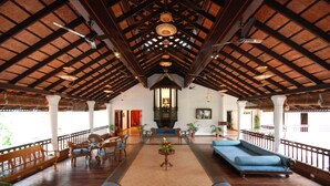 A spacious lobby with wooden flooring, a high ceiling with exposed beams, a central seating area with sofas and chairs, and a decorative chandelier. - The Raviz Kadavu (Kondotti)