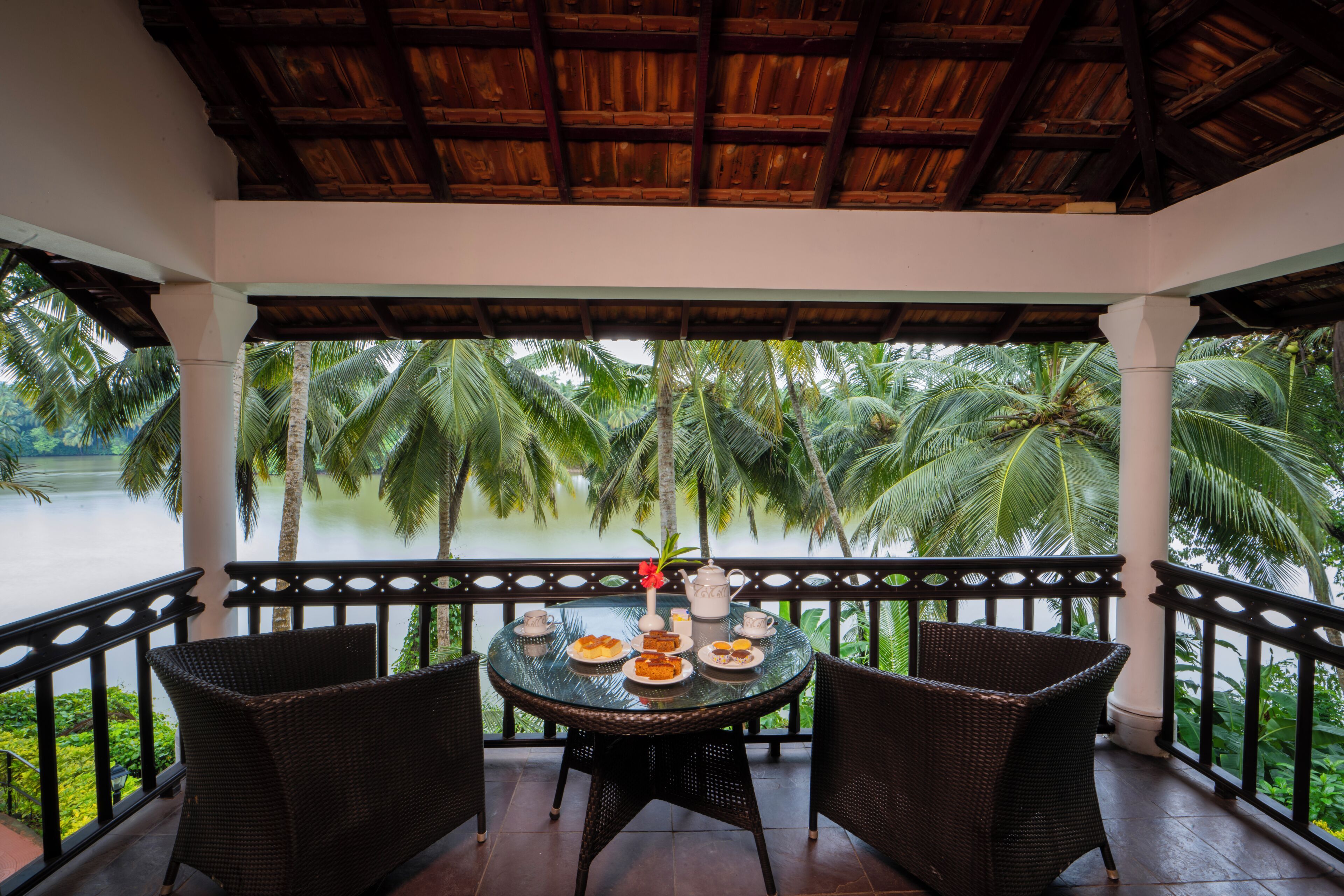 A covered outdoor seating area with a table set for a meal, overlooking a body of water and palm trees.