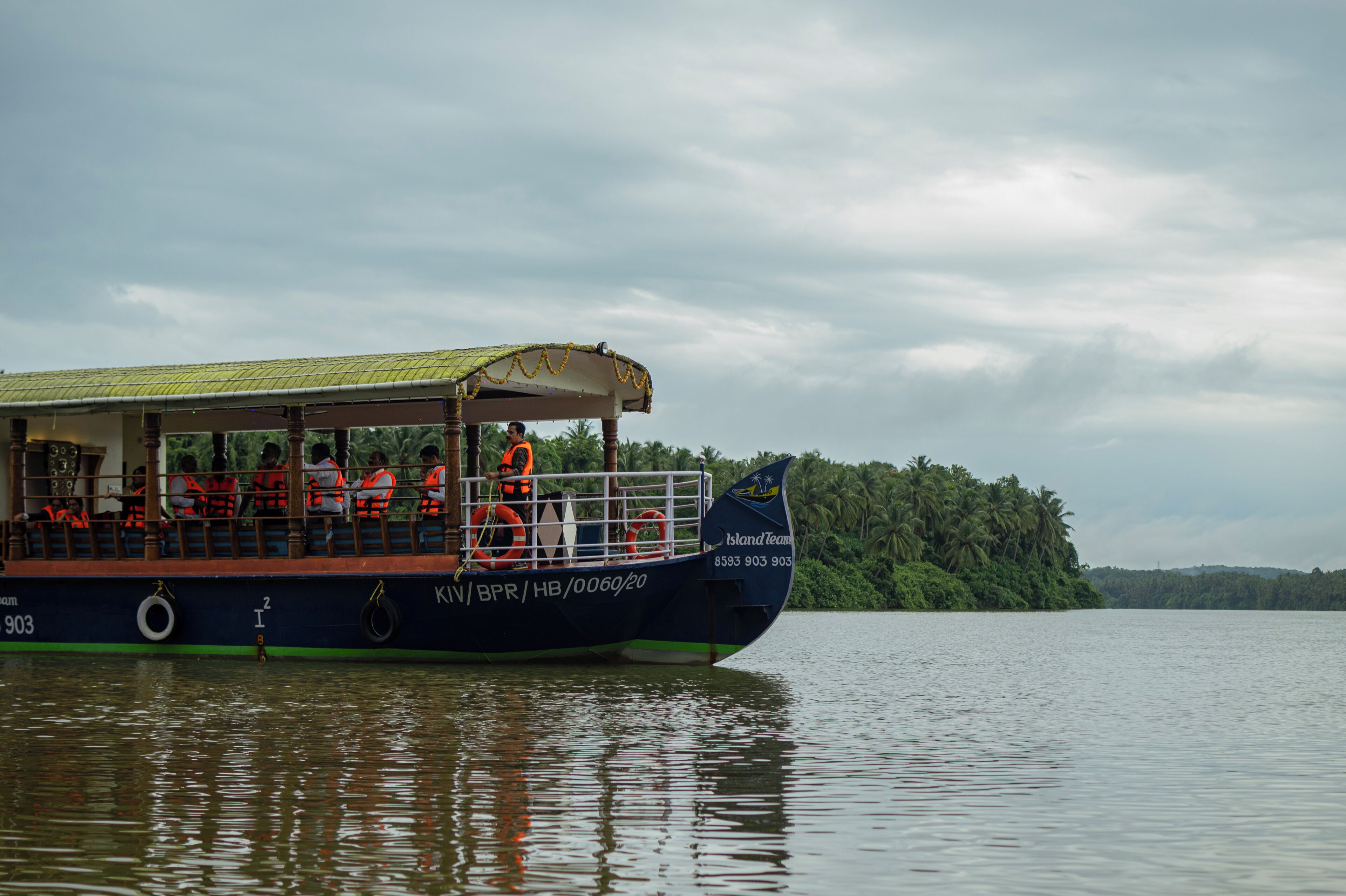 A boat with passengers wearing life jackets, a covered deck, and a green roof.