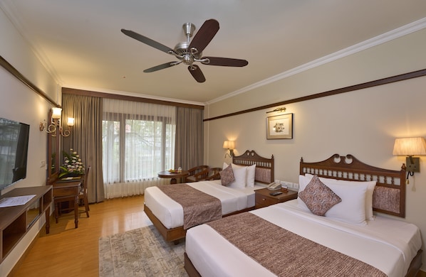 A hotel room with two beds, a ceiling fan, a desk with a chair, a TV, and a window with curtains.