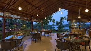 An outdoor dining area with tables and chairs, a bar, and a view of the sea. - The Raviz Kadavu (Kondotti)