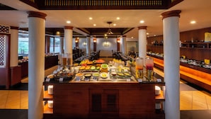 A buffet area with various food items and a beverage station, surrounded by wooden columns and a patterned ceiling. - The Raviz Kadavu (Kondotti)