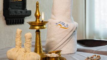 Une mise en scène traditionnelle avec une lampe à huile allumée, un pot rouge suspendu, un tissu blanc et un chapelet sur une table.