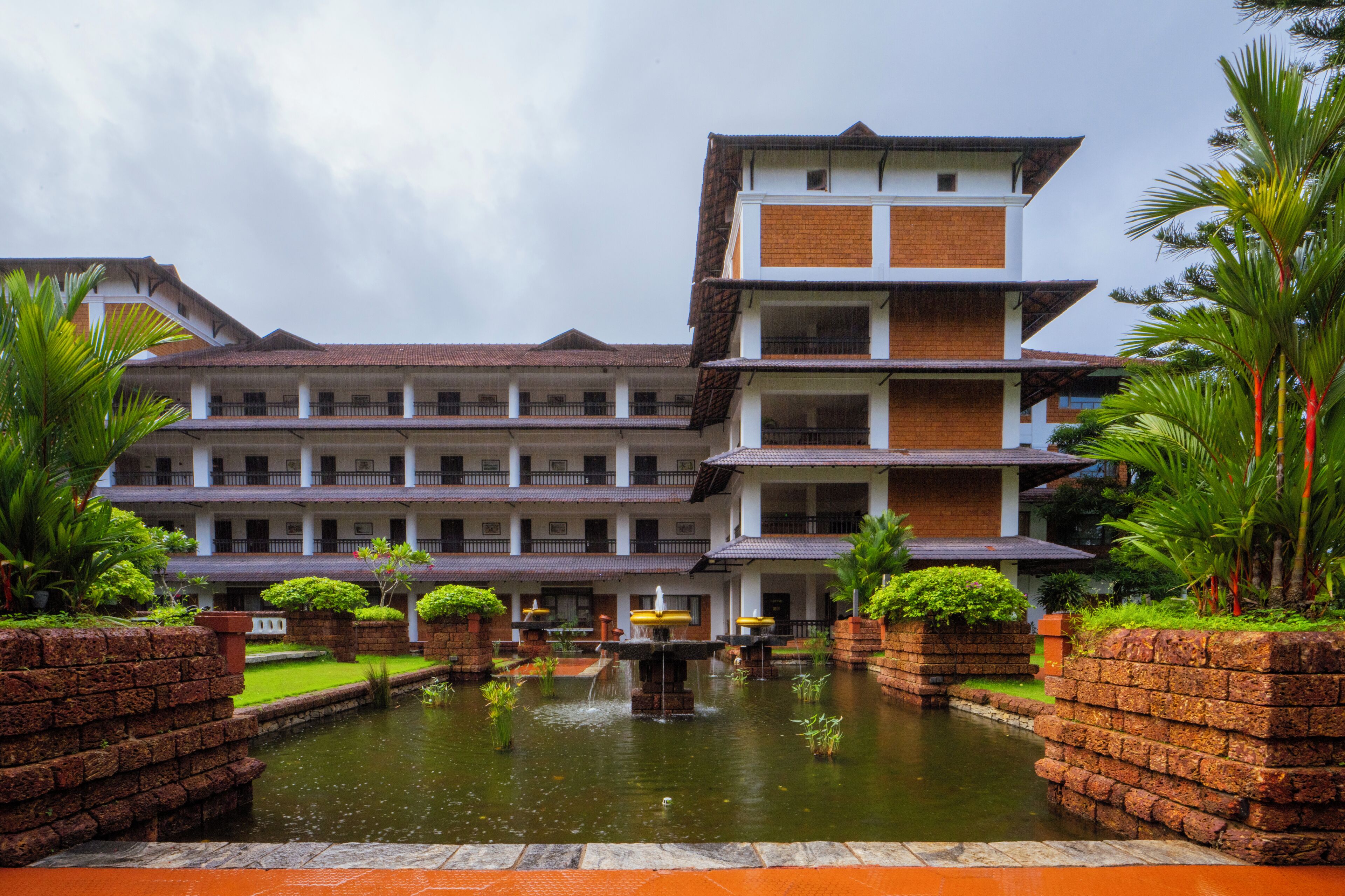 A multi-story hotel with a courtyard featuring a central water fountain, surrounded by brick walls and lush greenery.