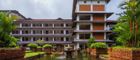 A multi-story hotel with a courtyard featuring a central water fountain, surrounded by brick walls and lush greenery.