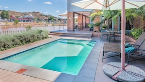 A swimming pool with a view of a hill and a body of water. There are lounge chairs and umbrellas around the pool area. - Town Lodge Roodepoort (Roodepoort)