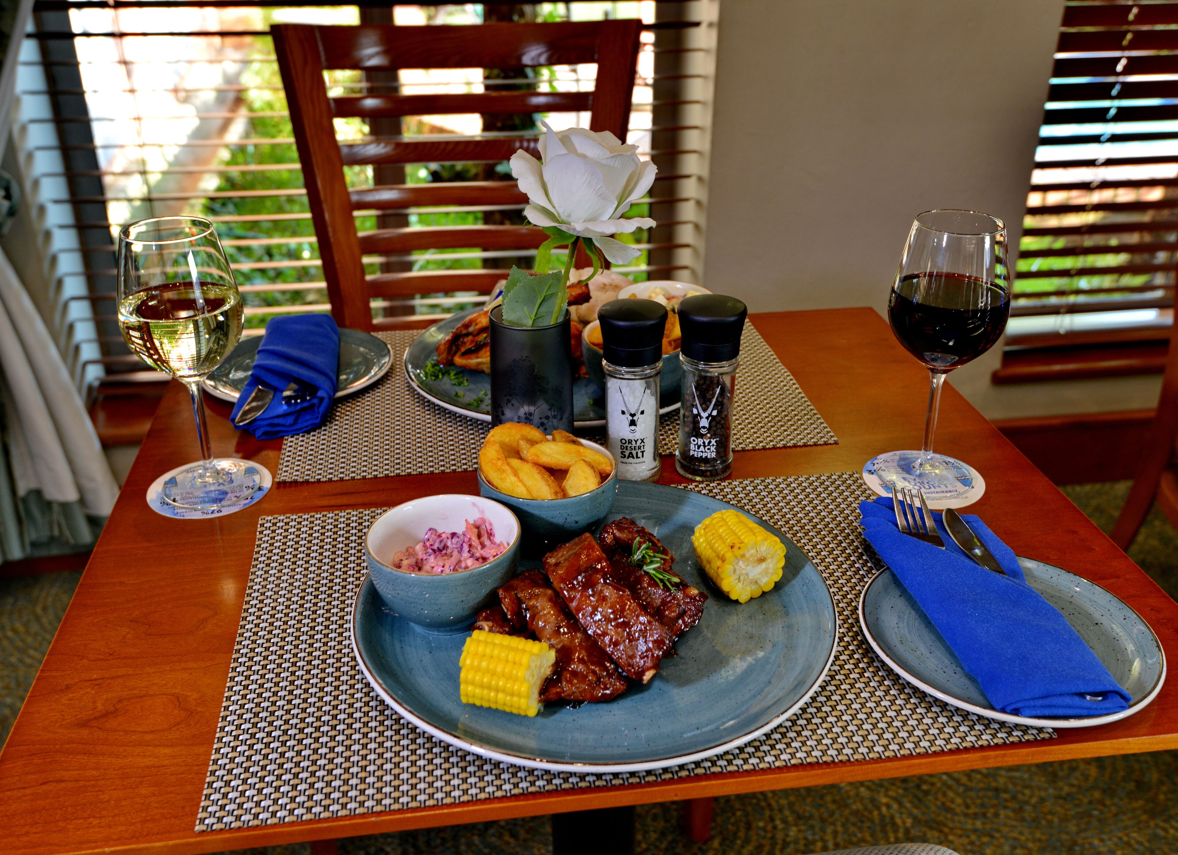 A dining table with a plate of food, a glass of white wine, and a glass of red wine.