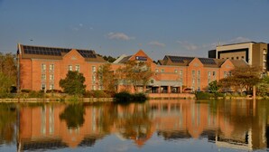 A brick building with solar panels on the roof, a sign reading "Town Lodge," and a calm body of water in front. - Town Lodge Roodepoort (Roodepoort)
