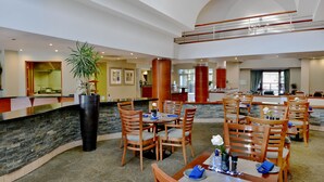 A spacious hotel lobby with multiple dining areas, a reception desk, and a large potted plant. - Town Lodge Roodepoort (Roodepoort)