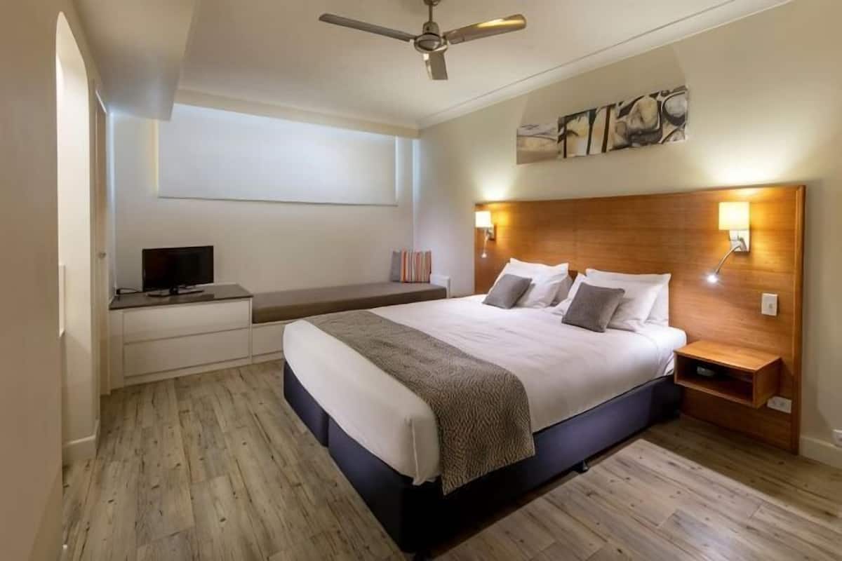 Ein Schlafzimmer mit einem Bett, Nachttischen, einem Fernseher, einem Deckenventilator und einem Wandbild.