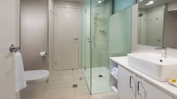 Een moderne badkamer met een douchecabine van glas, een wit toilet en een wastafel met spiegel.