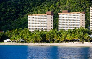A beachfront hotel with multiple high-rise buildings, palm trees, and a clear blue sea.