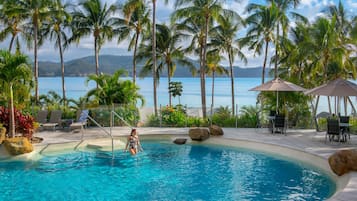 Una piscina al aire libre, sombrillas, sillones reclinables de piscina