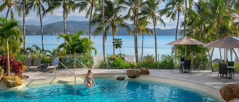 Una piscina al aire libre, sombrillas, sillones reclinables de piscina