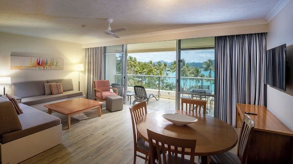 A hotel room with a balcony, a sofa, a table, and a TV. - Whitsunday Apartments (Whitsundays)