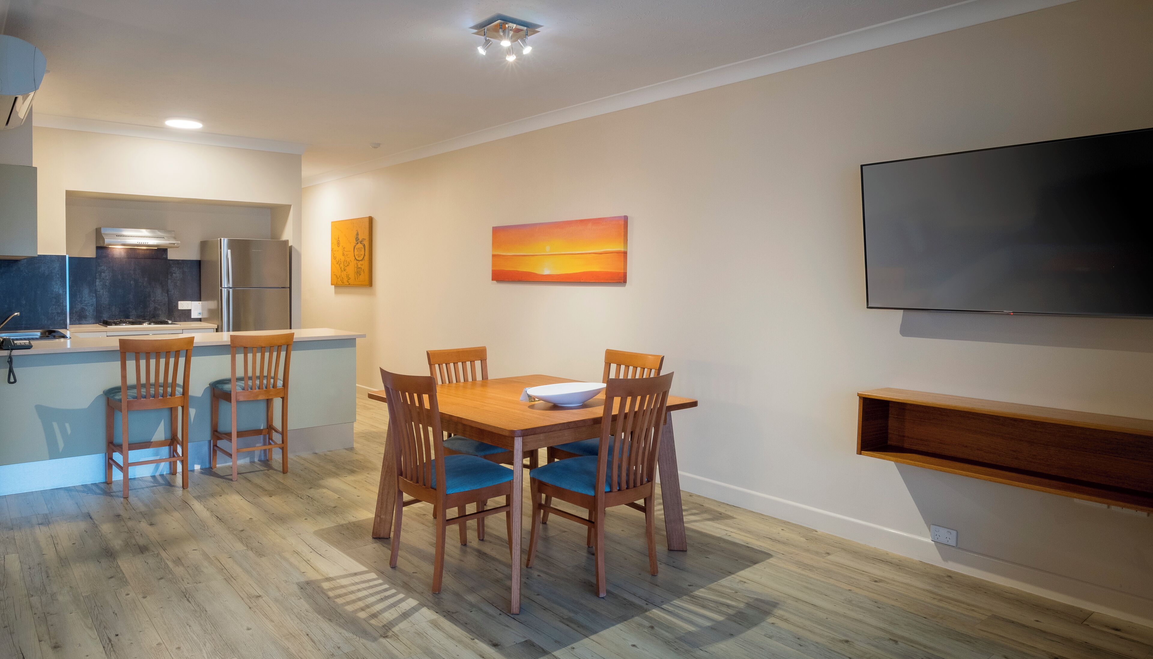 A modern kitchen with a dining area, a flat-screen TV, and artwork on the walls.