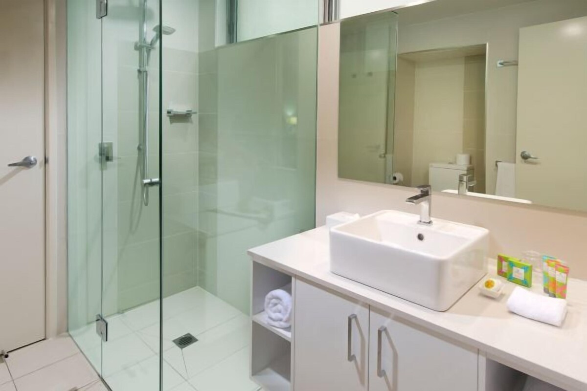 A modern bathroom with a glass-enclosed shower, a white sink, and a large mirror.