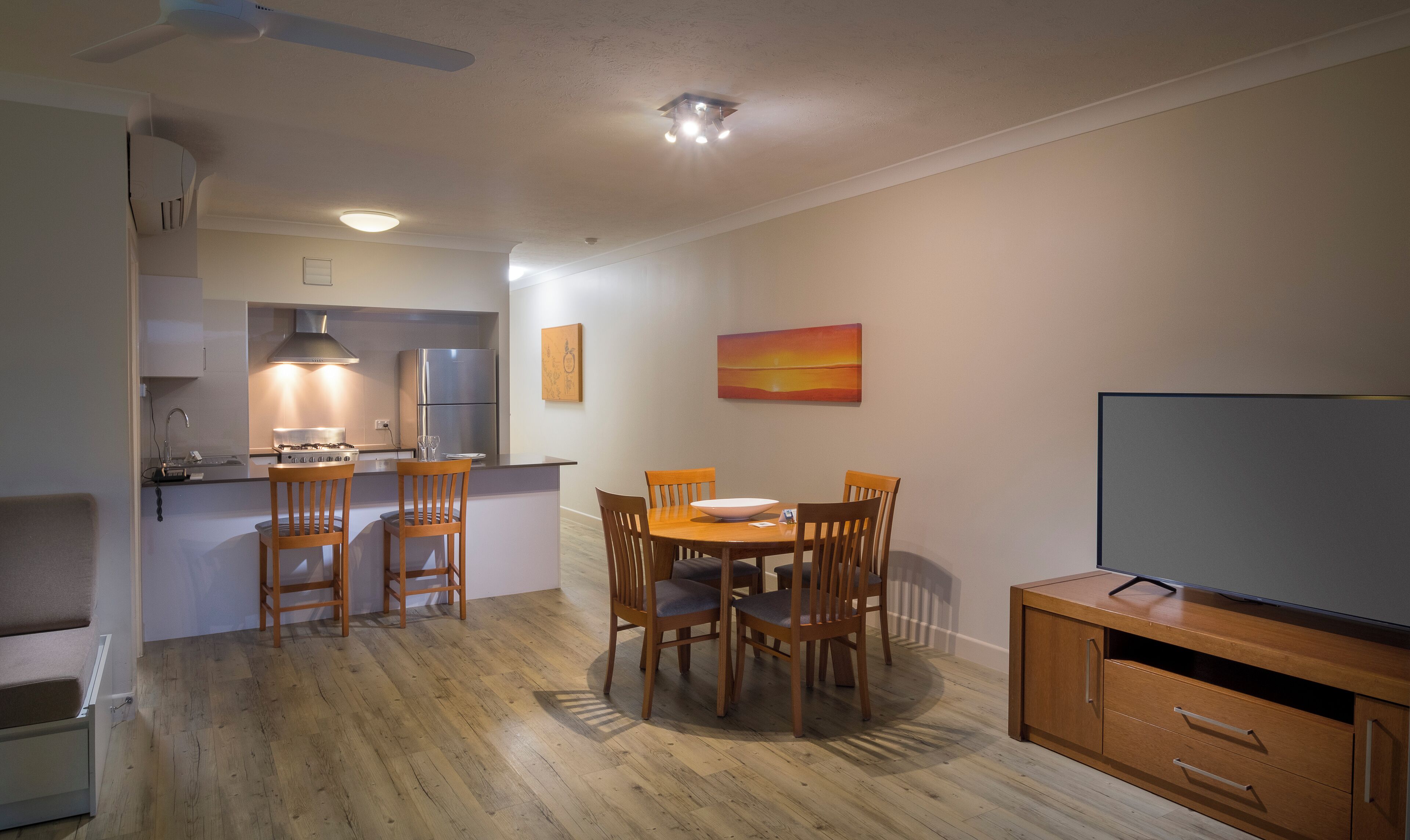 A compact kitchen with a dining area, a TV, and a painting on the wall.