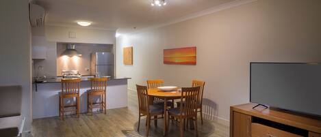 A compact kitchen with a dining area, a TV, and a painting on the wall.